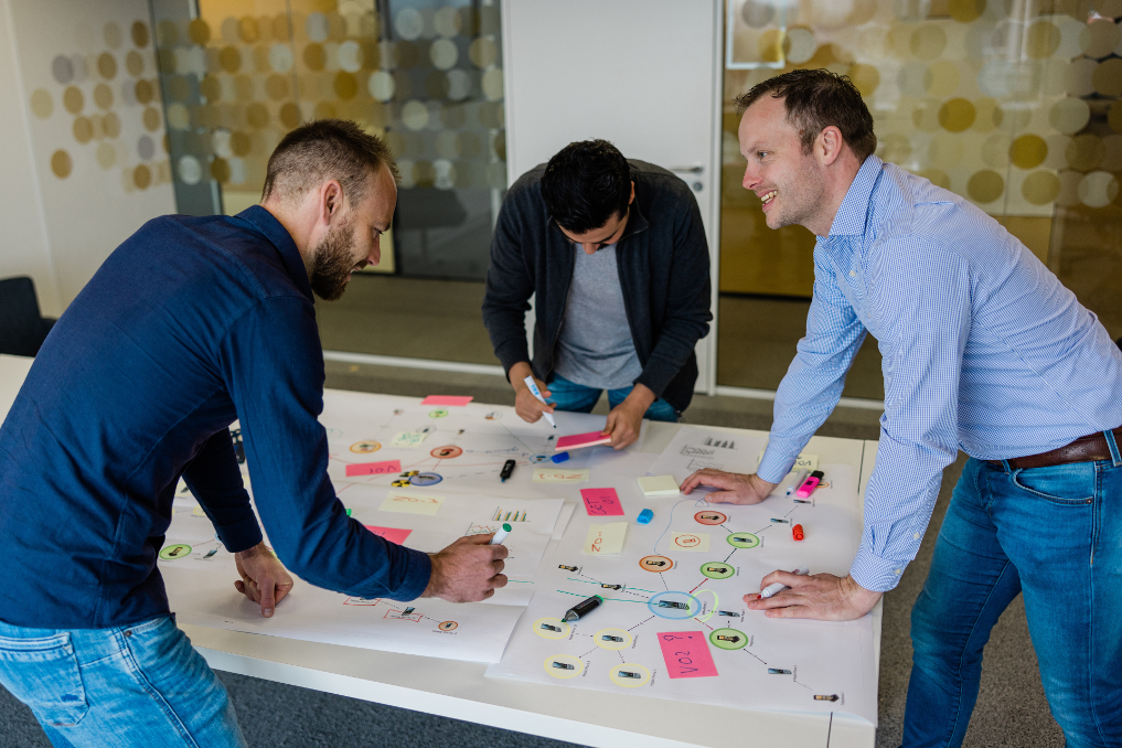 Collega's van het team intelligence overleggen rondom een tafel. Ze werken bij de Inlichtingen- en Opsporingsdienst van de Inspectie Leefomgeving en Transport