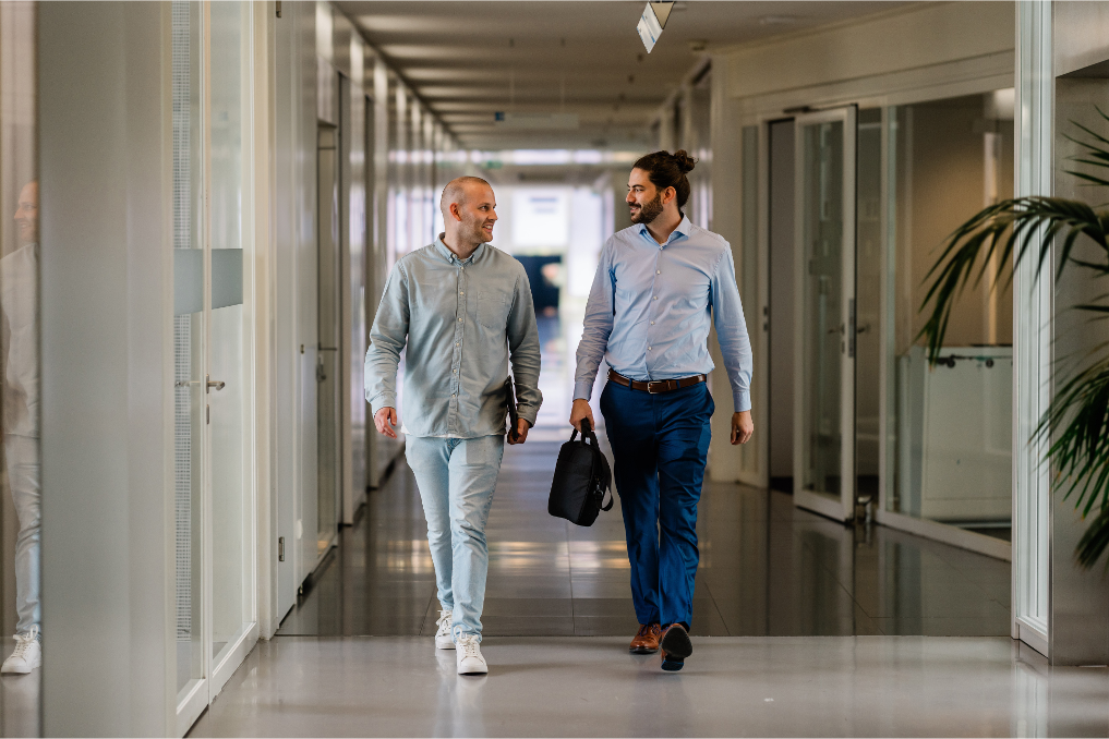 2 collega's bij de Inspectie Overheidsinformatie en Erfgoed lopen door de gang terwijl ze overleggen