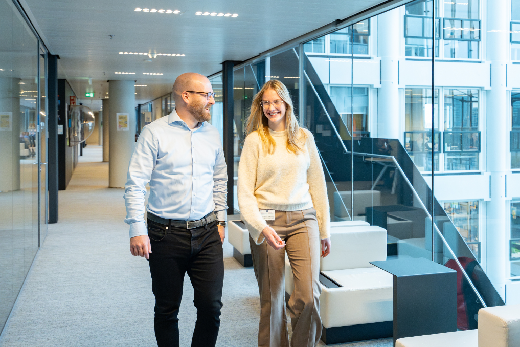 Wilco Ploeg loopt met een collega over de gang, lachend en pratend. Ze zijn juristen bij de Rijksoverheid